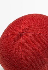 Cappello di lana rossa con una texture liscia, caratterizzato da una sommità arrotondata e cuciture sottili che si irradiano dal centro, creando una finitura ordinata.