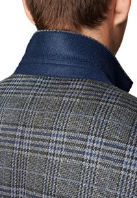 Wełniana kurtka z niebieskim filcowym kołnierzem. Szary wzór w kratę z czarnymi i niebieskimi akcentami. Teksturowany materiał widoczny w kołnierzu i korpusie.