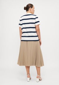 Marineblå og hvid stribet t-shirt med korte ærmer, parret med en plisseret beige midi-nederdel. Strappy hvide hæle fuldender outfittet.