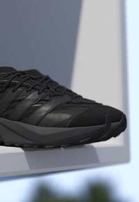 Par sorte atletiske sko med teksturerede detaljer og tykke såler placeret på en hvid overflade med blødt lys.