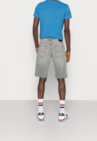 Shorts de mezclilla gris con un ajuste holgado, presentan bolsillos traseros y un dobladillo deshilachado. Combinados con una camiseta de manga corta azul y zapatillas blancas.
