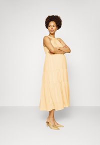 Vestido midi em amarelo em camadas, com tecido texturizado. Design sem mangas e corte descontraído. Usado com sapatos de salto fino em amarelo pálido.