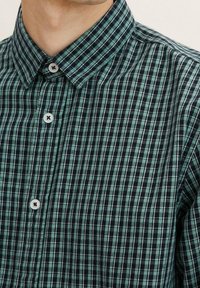 Camicia a quadri verde e navy con design a colletto, caratterizzata da bottoni bianchi e pattern a contrasto in una texture tessuta.