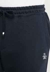 Navy blue sweatpants made of cotton blend fabric with a textured finish, featuring an elastic waistband and white penguin logo detail.