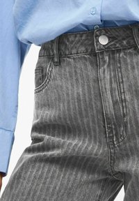 Pantalones de mezclilla a rayas grises con cintura alta, que cuentan con un cierre de botón frontal, pasadores para cinturón y bolsillos laterales, combinados con una camisa azul clara.