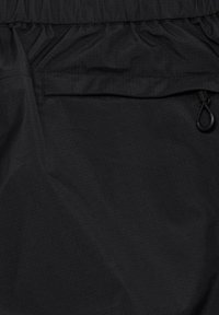 Tessuto nero con una tasca orizzontale con cerniera dotata di cordino e vita elasticizzata arricciata sopra la tasca.