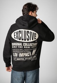 Black hoodie with a spacious hood, featuring large white text on the back. Material appears soft and durable, with a loose fit.