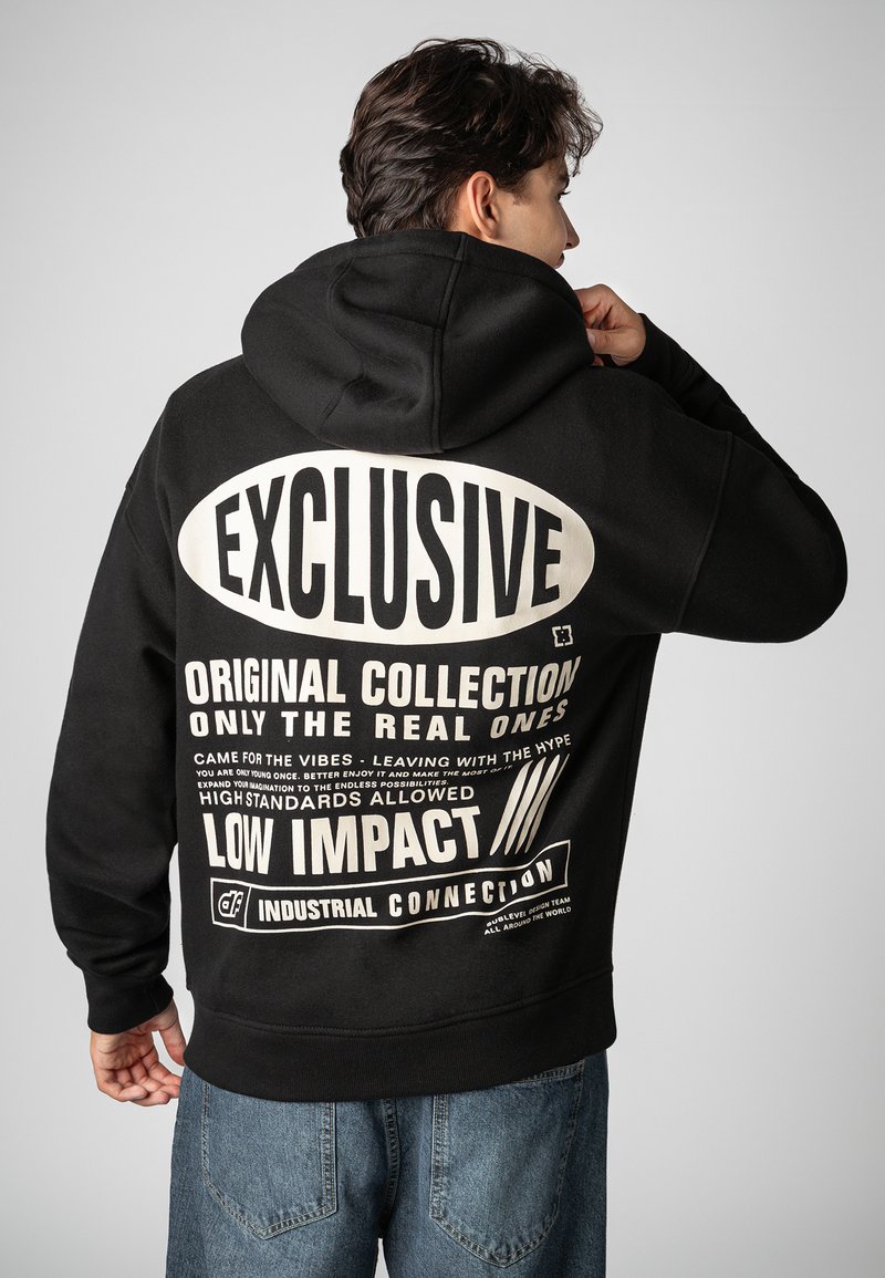 Black hoodie with a spacious hood, featuring large white text on the back. Material appears soft and durable, with a loose fit.