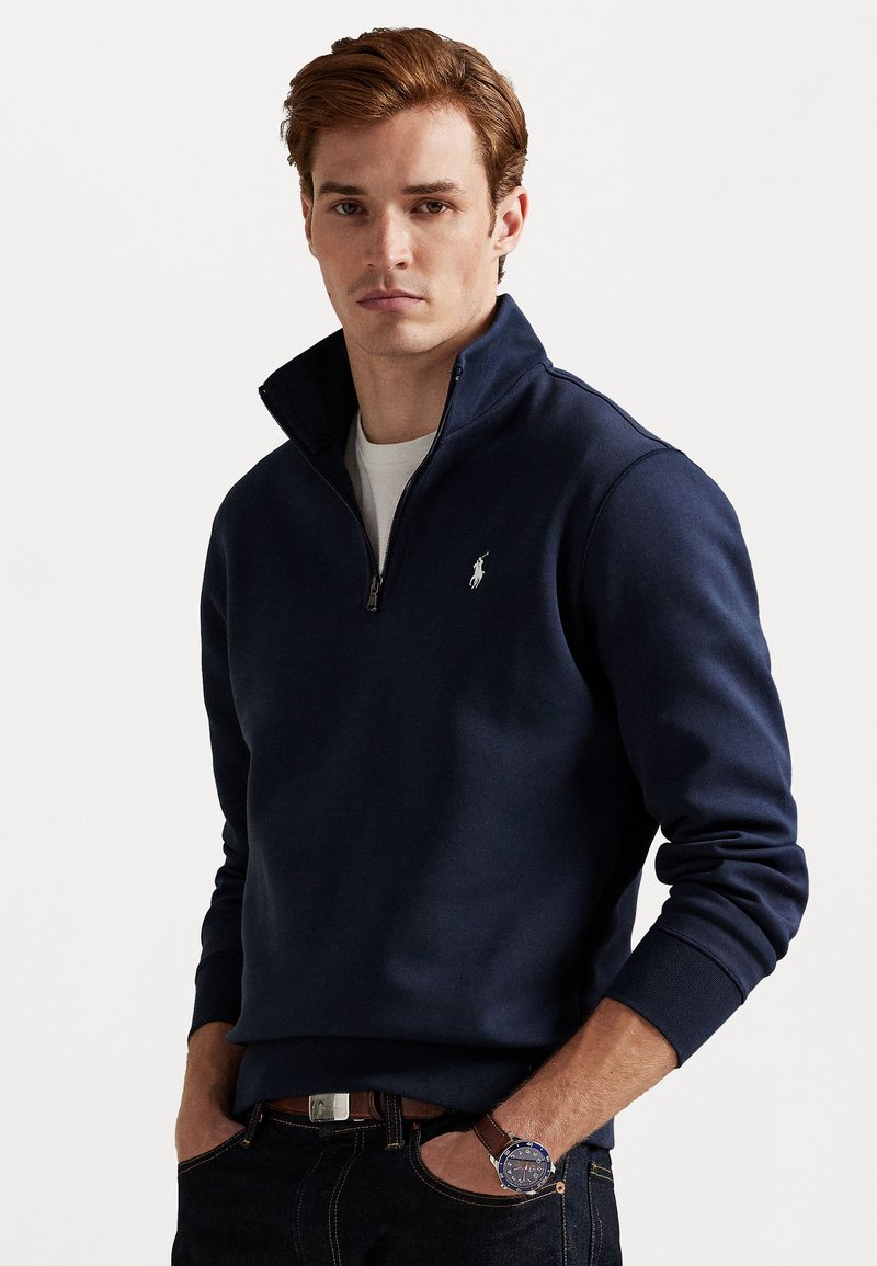 Marinefarvet zip-up sweatshirt lavet af blandet bomuld med ribbede manchetter og kant. Har et lille broderet logo på venstre bryst. Båret med mørke jeans og et ur.