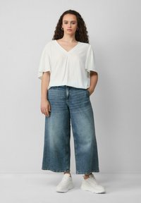 Biała bluzka w serek z krótkimi, szerokimi rękawami połączona z luźnymi, jasnoniebieskimi spodniami typu wide-leg i białymi trampkami. Prosty i casualowy design.