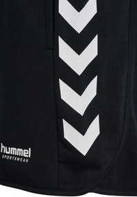 Schwarze Sportbekleidung mit einem markanten weißen Chevronmuster an der Seite und dem Markennamen "hummel" in Weiß.