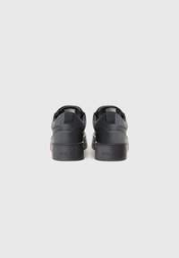 Black sneakers with a smooth leather upper, round toe, padded collar, flat laces, and a thick rubber sole. Rear pull tab for easy wear.
