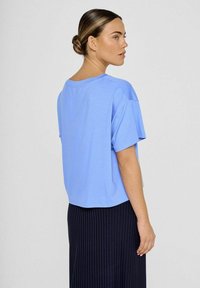 Lysblå kortærmet t-shirt med en afslappet pasform, rund halsudskæring og blød tekstur, parret med en mørk plisseret nederdel.