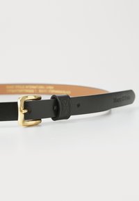 Svart lærbelte med en gullfarget metallspenne, utstyrt med debossert logo og en glatt finish. Baksiden er i brun med trykt tekst.