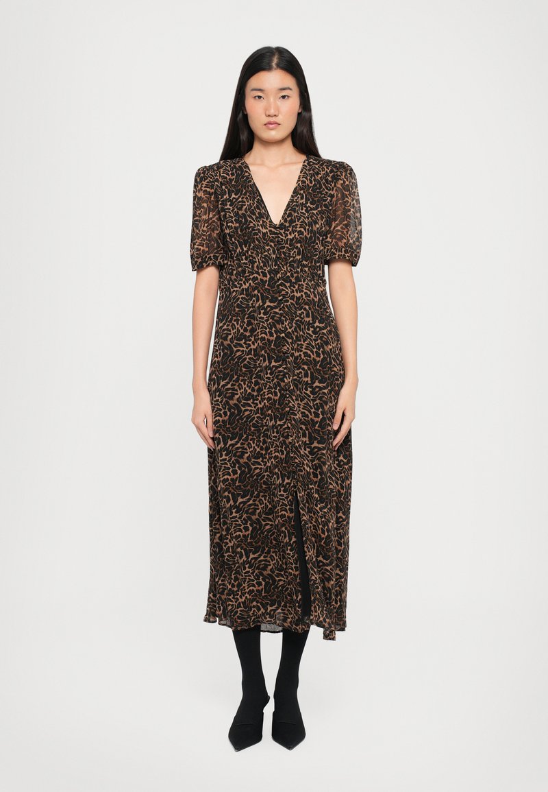 Svart kjole med et brunt abstrakt mønster, v-hals, pufferm, og splitt. Modellen har på seg svarte leggins og spisse sko.