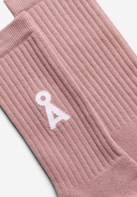 Chaussettes côtelées rose clair avec un logo blanc sur le côté. Fabriquées en tissu doux avec une finition texturée pour un confort optimal.