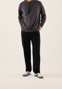 Ciemnoszara bluza z kapturem i sznurkami, zestawiona z czarnymi spodniami i szarymi butami z białymi paskami. Gładka tekstura i luźny krój.