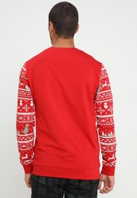 Punainen neulepaita, jossa on pitkät hihat ja jouluteemainen kuviointi, johon kuuluu poroja ja lumihiutaleita, valmistettu pehmeästä kankaasta. Selkäosa on yksivärinen punainen.