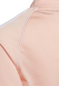 Polo de color melocotón claro con una textura suave, acentos de costura blanca y un diseño de cuello clásico con un brillo sutil.