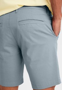 Pantaloni corti azzurri chiari in cotone con una texture liscia. Presentano due tasche posteriori e un taglio dritto all'orlo.