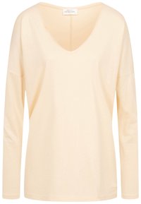 Ljus persikofärgad långärmad topp med djup V-ringning, tillverkad av mjukt material. Har en avslappnad passform och subtila sömmar längs kanten.