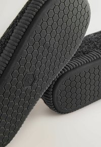  Sorte slip-on sko med en struktureret, hexagonal mønstret sål og ribbet kantdetalje. Materialet ser blødt og holdbart ud. Størrelse 8 ½.