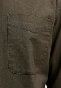 Olijfgroene shirt met een linkse borstzak. De stof heeft een gladde textuur met een effen patroon en subtiele stiksels.