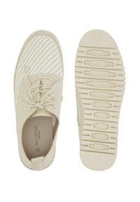 Zapatos de color beige claro con parte superior de tejido trenzado, detalles en cuero suave, punta redondeada y suela de goma texturizada con patrones de agarre.