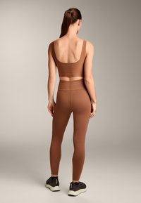 Barna sportos szett, amely egy ujjatlan crop toppból és magasderekú leggingsből áll. Simább textúra, minimális márkázás és támogató kialakítás jellemzi.