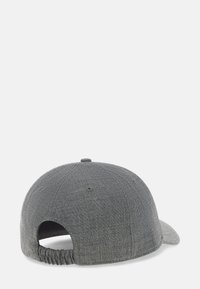 Pelēka auduma beisbola cepure redzama no aizmugures ar elastīgu siksnu un ventilācijas caurumiem uz balta fona.