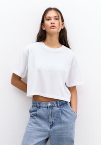 Tricou alb scurt, cu mâneci scurte, din bumbac moale. Asortat cu blugi de talie înaltă, de culoare albastru deschis, cu închidere prin buton și buzunare laterale.