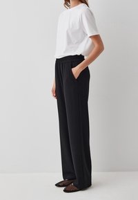 Zwarte wijde broek met elastische tailleband en zijzakken, gecombineerd met een witte T-shirt met ronde hals en zwarte mesh puntige flats.
