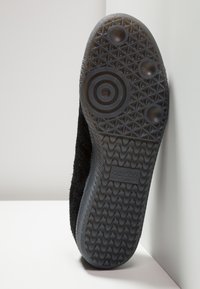 Baskets noires avec une tige en tissu texturé et une semelle en caoutchouc. Présente des motifs circulaires et de relief au fond, avec le détail du logo "adidas".