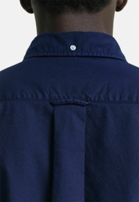 Camicia blu navy con piega sul retro e bottone al colletto. Realizzata in un tessuto morbido con un design strutturato e dettagli minimalisti.