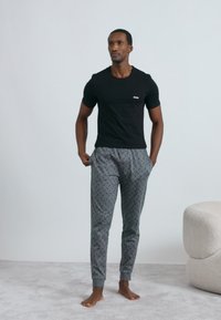 Maglietta nera a girocollo con piccolo logo bianco, abbinata a pantaloni della tuta grigi con motivo geometrico e polsini elastici.