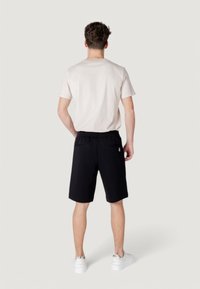 Black shorts with elastic waistband and back pockets, paired with a light beige T-shirt. The model is wearing white sneakers.
