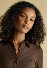 Brown ribbed blouse with a collared neckline and button placket. Features soft texture and fits close to the body, accentuating the silhouette.