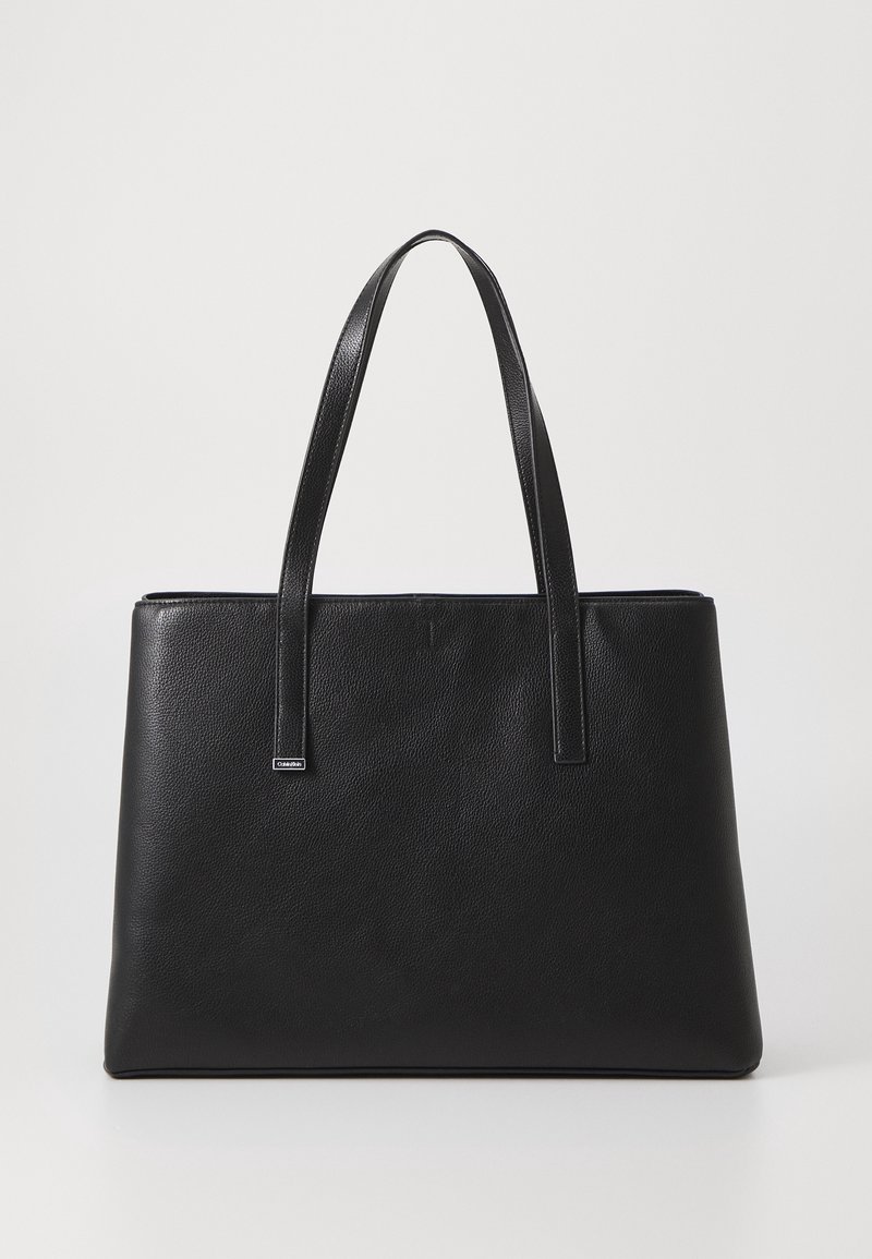 Sac cabas en cuir noir texturé avec deux bretelles et une petite étiquette métallique de marque sur une bretelle.