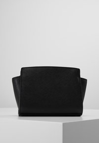 Černá kožená kabelka s texturovaným povrchem, obdélníkovým tvarem a ostrými stranami. Obsahuje jemné prošívání podél okrajů.