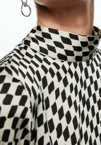 Schwarzes und weißes gemustertes Oberteil mit hohem Kragen und einem glatten, leichten Stoff mit geometrischer Textur.