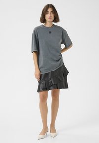 Tricou supradimensionat gri, cu mâneci scurte, având un guler rotund și detalii brodate, asortat cu o fustă din piele ecologică neagră cu volane.