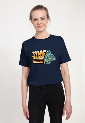 Navy blue t-shirt featuring a cartoon stegosaurus and yellow text reading "TIME TRAVELLER FROM ANOTHER WORLD JURASSIC PORTAL."