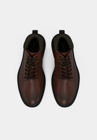 Braune Lederschuhe mit runden Zehen, braunen Schnürsenkeln und schwarzen Gummisohlen. Verfügen über ein niedriges Knöchellayout und eine Zuglasche an der Ferse.