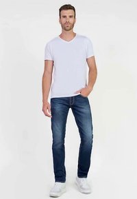 T-shirt bianca a V abbinata a jeans slim fit blu scuro. L'outfit include sneakers bianche e presenta una vestibilità comoda e un design semplice.