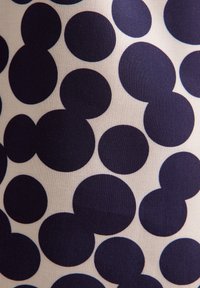 Cerchi blu navy di diverse dimensioni su un tessuto crema chiaro. Il motivo presenta linee morbide e una texture delicata, creando un design giocoso.