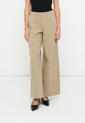 Pantalons beige à jambes larges en tissu doux, avec une taille haute, deux poches avant et une fermeture à bouton unique. Texture lisse, silhouette droite.