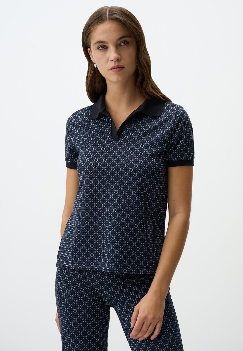 Marineblauwe polo met een gemusterd design, korte mouwen en een donkere kraag; gecombineerd met bijpassende gemusterde broek. Soepele textuur, casual fit.