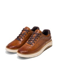 Hnědé kožené tenisky s tmavě hnědými tkaničkami, polstrovaným límcem a bílou gumovou podrážkou. Obsahují jemné švy a detail loga.