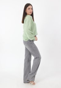 Mintgrüner Strickpullover mit lockerer Passform und grauen Schlagjeans. Das Outfit zeichnet sich durch eine glatte Textur und dezente Muster aus.
