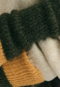 Szydełkowy szalik z trzema sekcjami: oliwkowa zieleń, musztardowa żółć i kremowy. Miękka faktura z różnymi wzorami ściegów i warstwowym wyglądem.